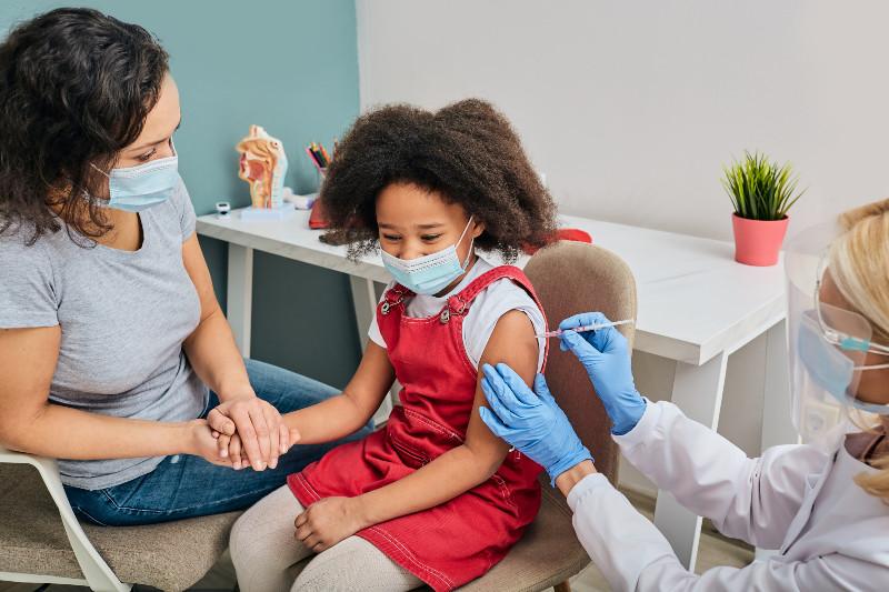 a young girl getting a shot while holding her moms hand