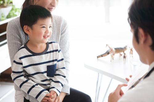 a boy sitting on his moms lap talking to a doctor