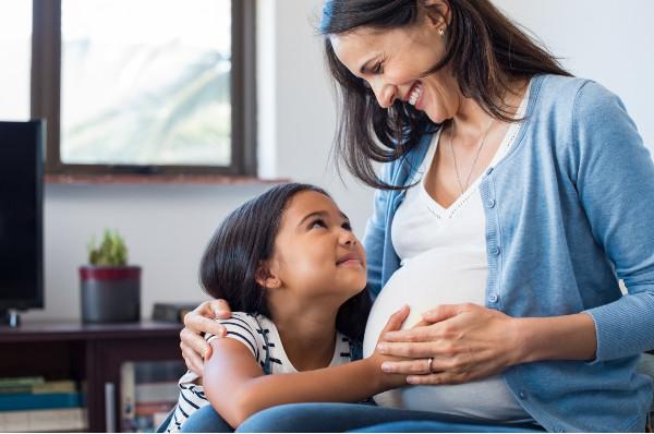 a girl touching her mom's pregnant stomach and both smiling