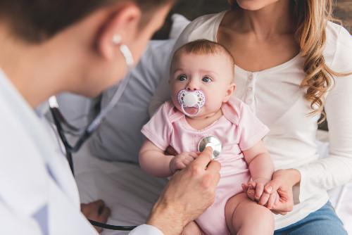 a very cute baby on her mom's lap while a doctor listens to her heart